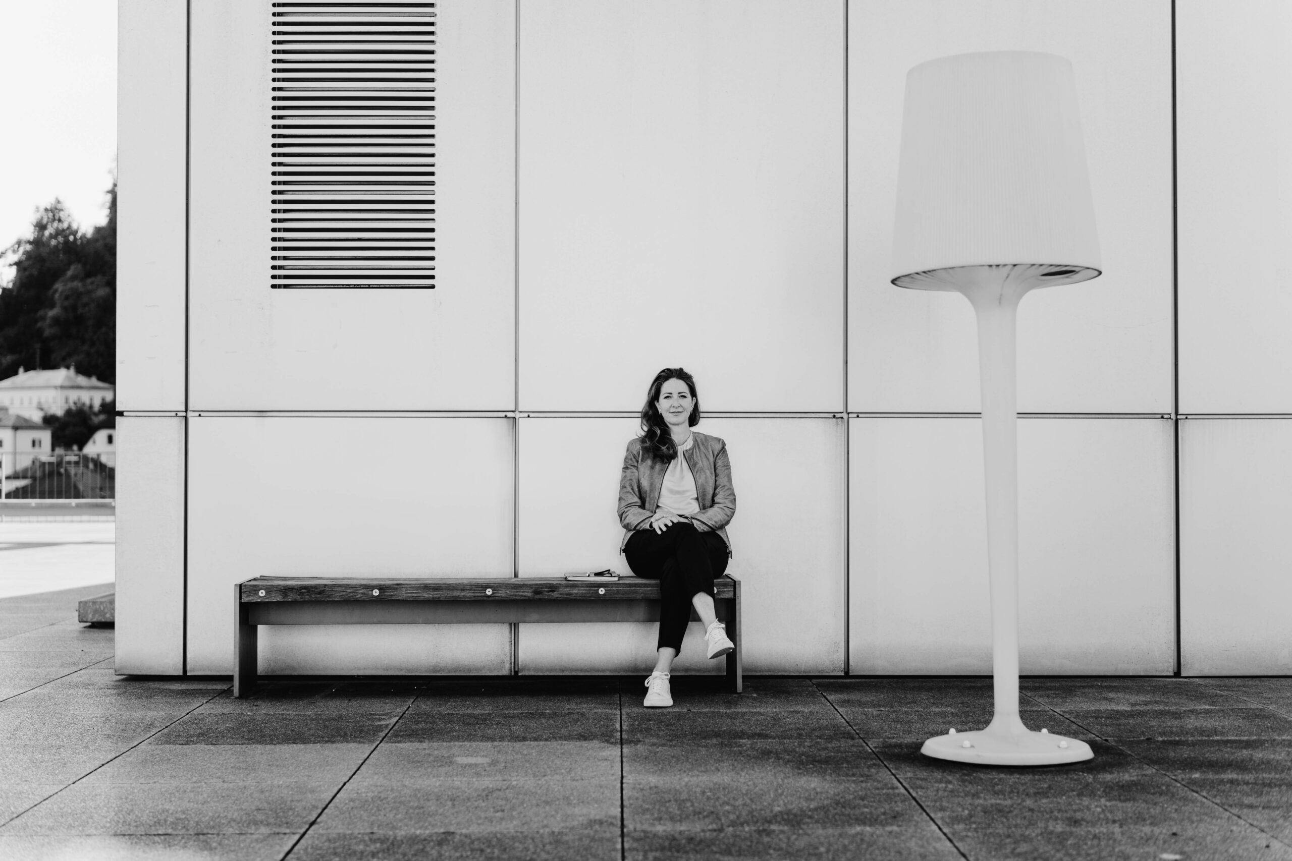 Ute Zischinsky, Female Leadership Coach Frau sitzt entspannt auf einer Bank vor heller Wand und lächelt.